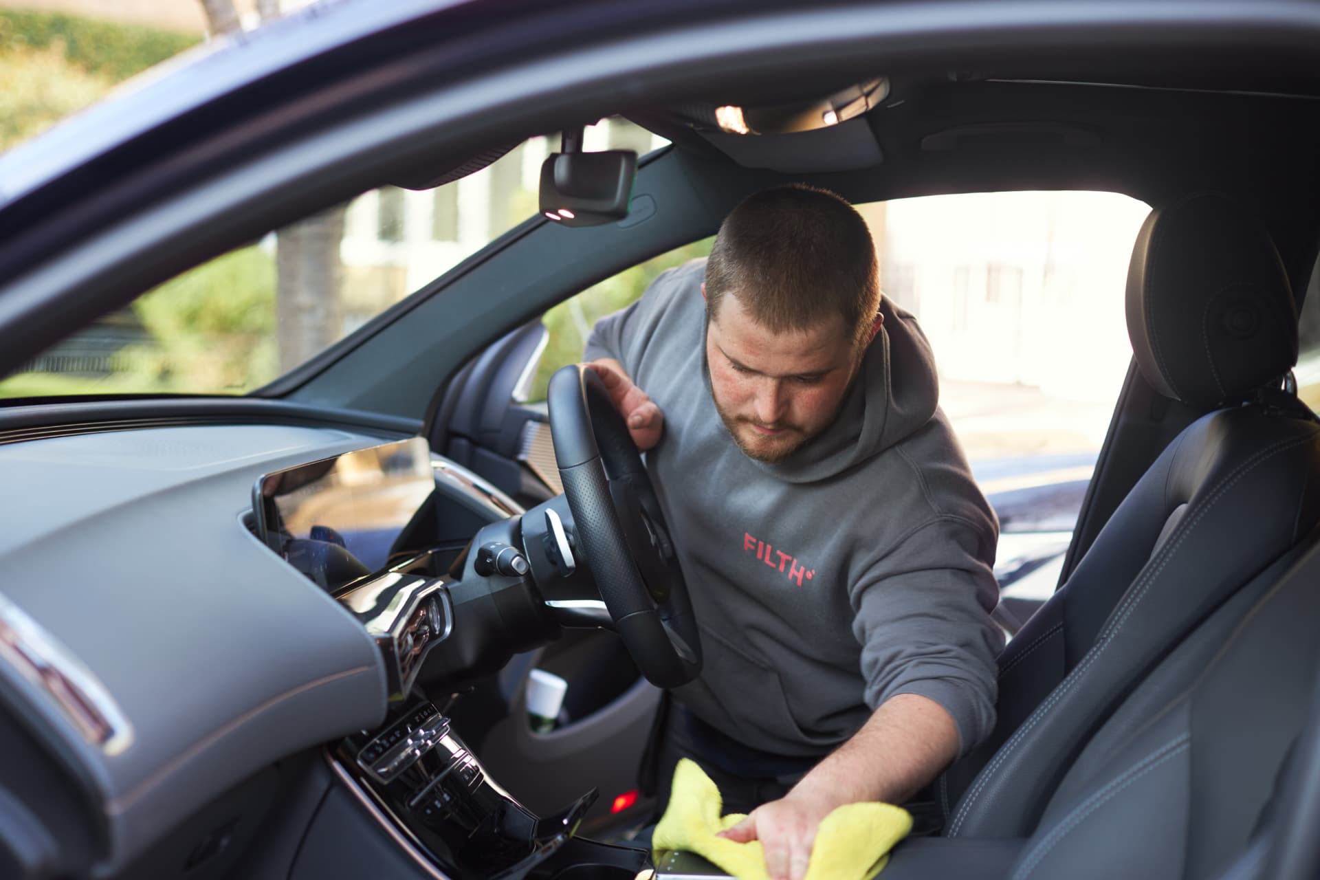 Filth technician cleaning a car interior with a microfibre cloth